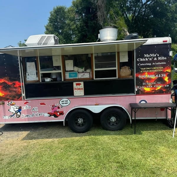 MeMa’s Chick’n & Ribs catering food truck parked on grass, decorated with barbecue graphics, picnic tablecloth trim, and menu windows.