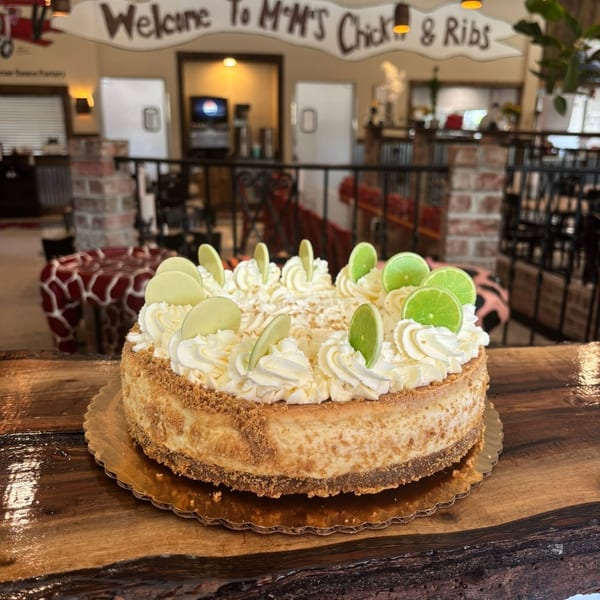 Key lime cheesecake topped with whipped cream and lime slices on a wooden table inside M K’s Chicken & Ribs restaurant.